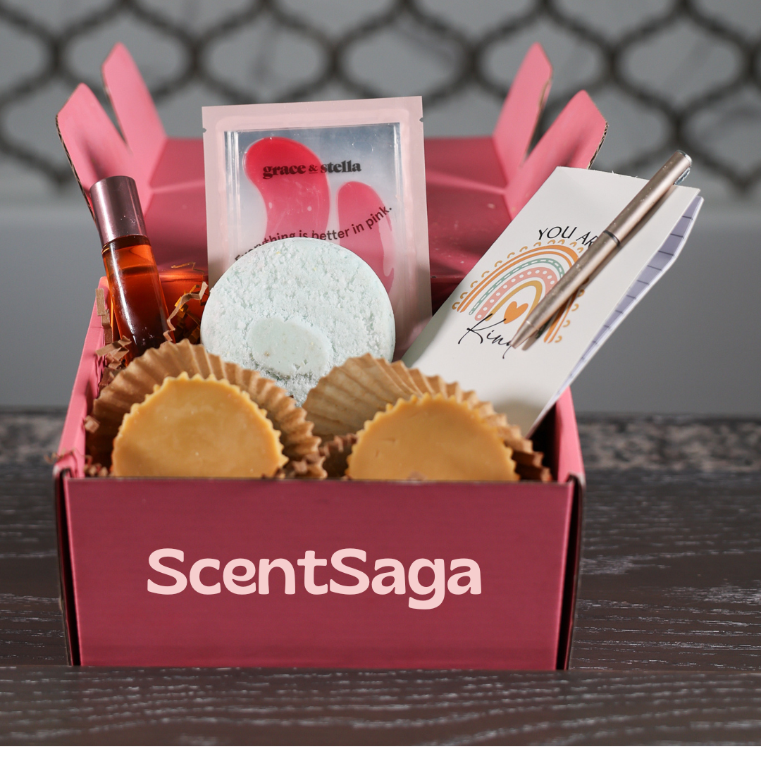 A pink subscription box brimming with luxurious self-care products, including wax melts, candles, lotion bars, soap, perfume, a mini notebook, a pen, and more. Set on a wooden table with a blurred white background, this elegant display highlights the perfect assortment for indulging in your self-care routine.