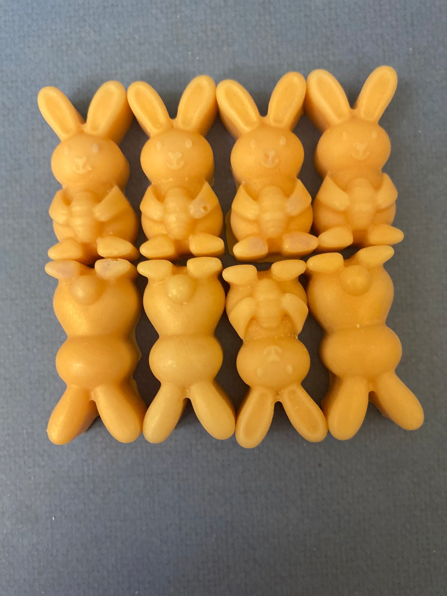 Eight orange-colored bunny-shaped soy wax melts arranged on a light purple flat surface, creating a vibrant and cheerful display that embodies playful and uplifting vibes.