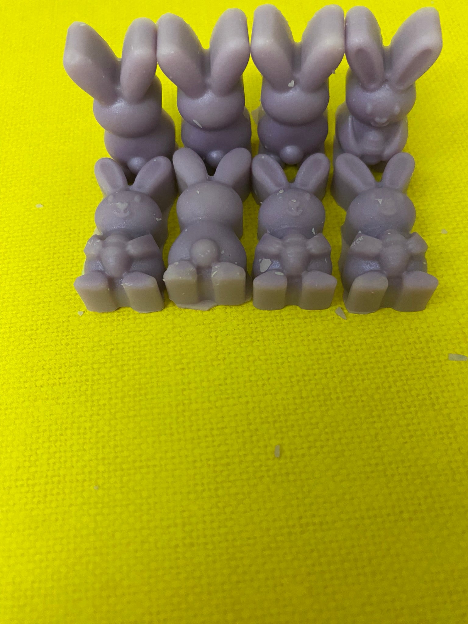 Eight purple-colored bunny-shaped soy wax melts arranged on a yellow flat surface, creating a vibrant and cheerful display that embodies playful and uplifting vibes.