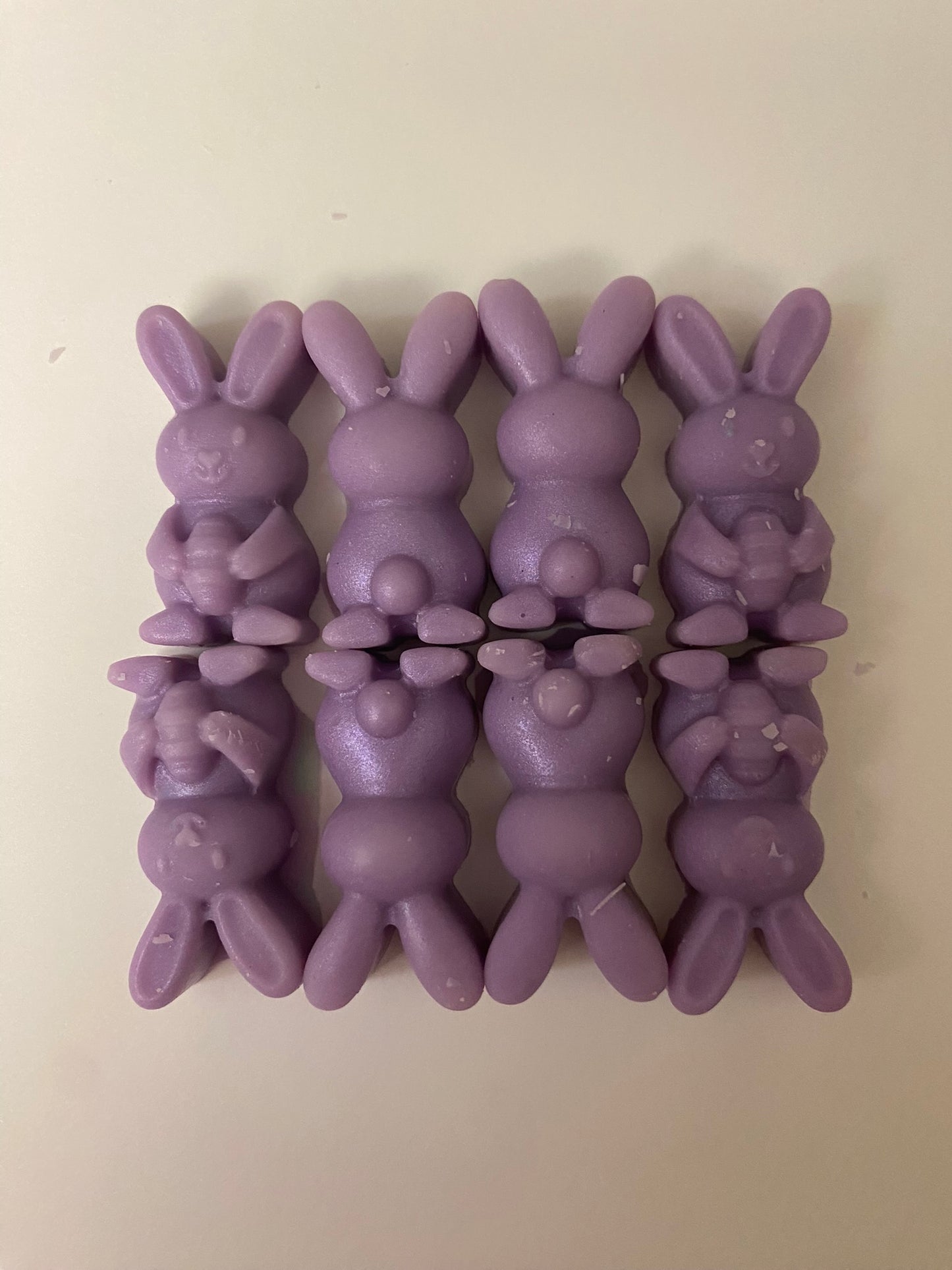 Eight purple-colored bunny-shaped soy wax melts arranged on a light pink flat surface, creating a vibrant and cheerful display that embodies playful and uplifting vibes.