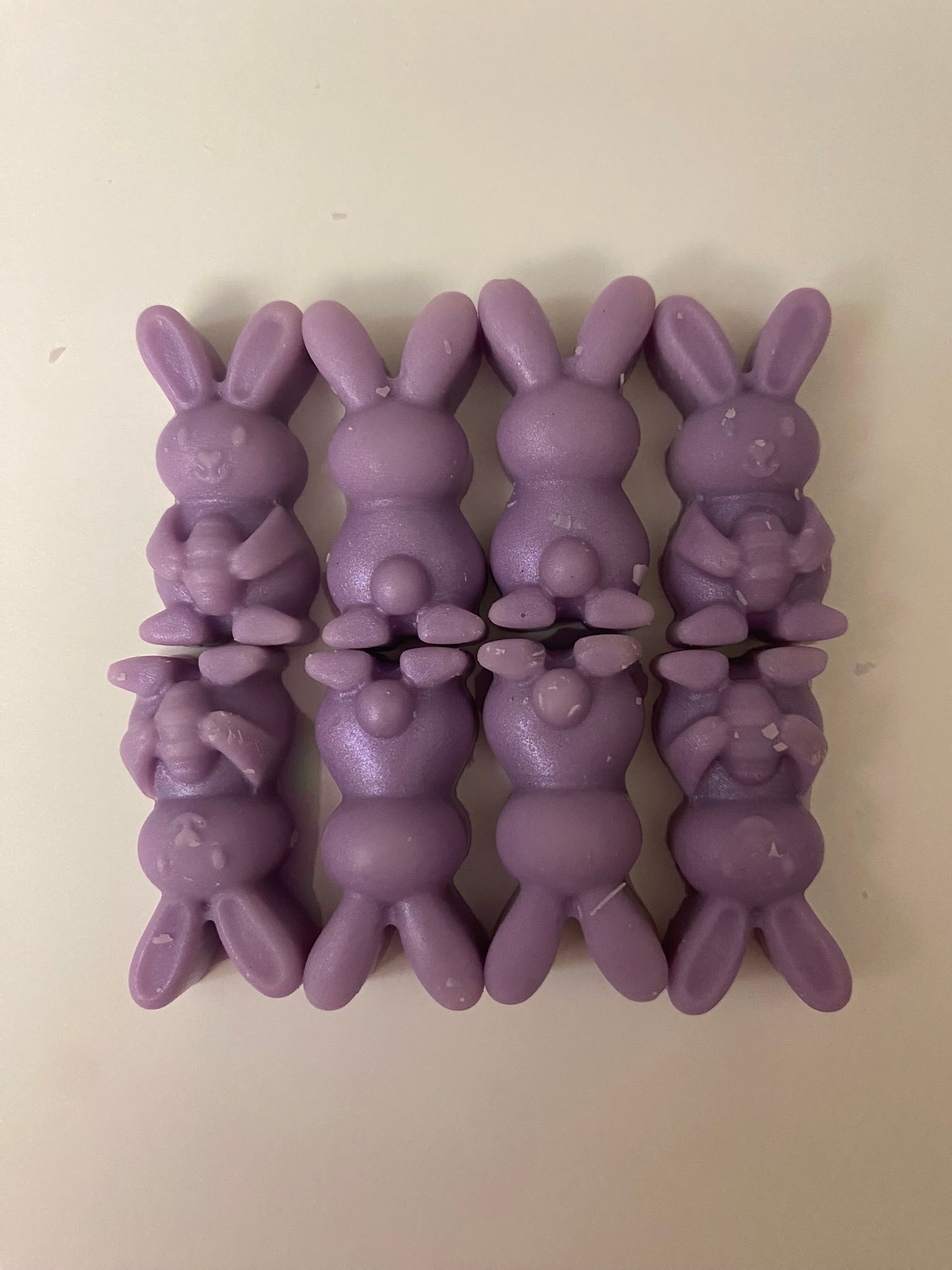 Eight purple-colored bunny-shaped soy wax melts arranged on a light pink flat surface, creating a vibrant and cheerful display that embodies playful and uplifting vibes.