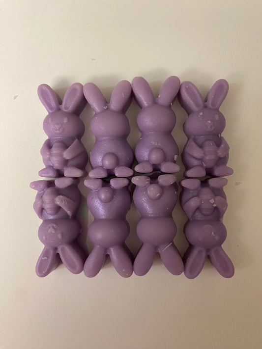 Eight purple-colored bunny-shaped soy wax melts arranged on a light pink flat surface, creating a vibrant and cheerful display that embodies playful and uplifting vibes.