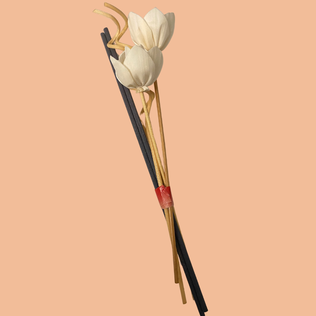 A stylish reed diffuser paired with two pieces of white flowers, set against a soft pink background. The setup exudes elegance and sophistication, adding a touch of charm to your space.