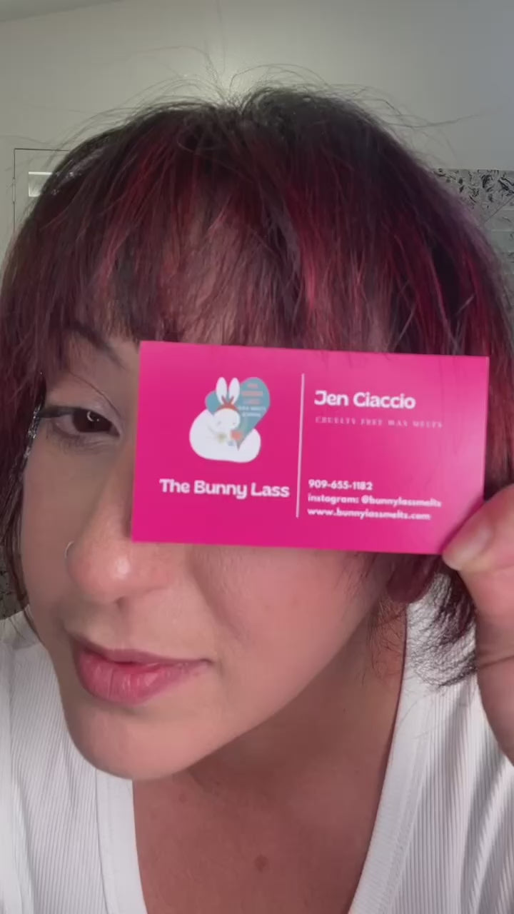 Video of a cheerful girl holding a pink subscription box filled with luxurious self-care products like candles, wax melts, lotion bars, soap, perfume, a mini notebook, and a pen. She excitedly opens the box, showcasing each item while sitting at a cozy wooden table. The background is a soft white, emphasizing the products and her joy, as she shares how the box is perfect for elevating your self-care routine.