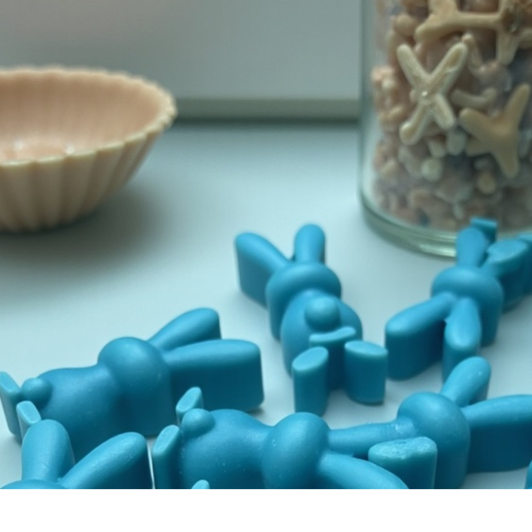 Ocean-inspired bunny-shaped wax melt scented candle in ocean-themed colors alongside a jar filled with ocean sand and shells behind it and a bowl shaped like a shell.