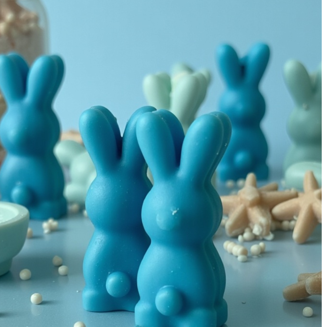 Ocean-inspired bunny-shaped wax melt scented candle in ocean-themed colors, with white pearls and starfish in the background, and a jar filled with ocean sand and shells behind it.