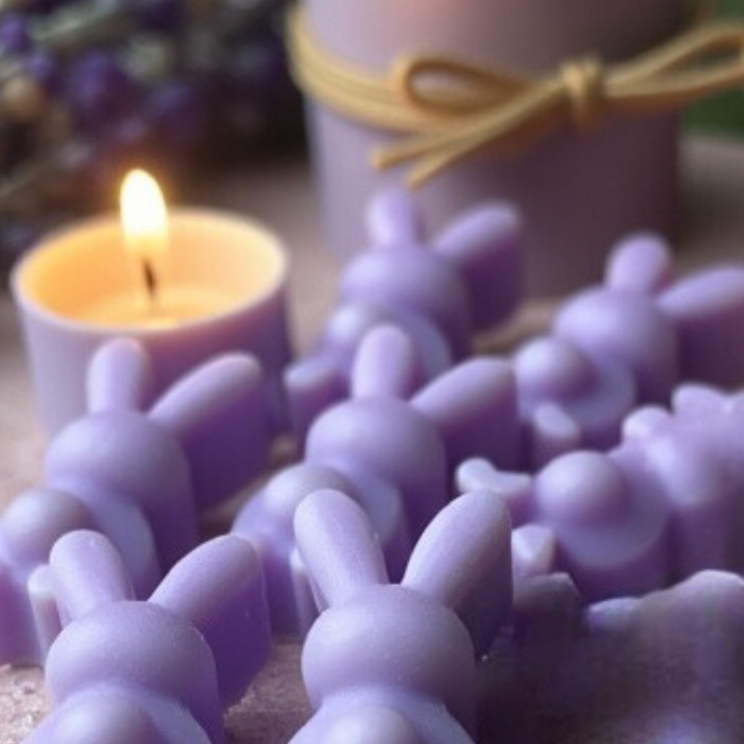 Close-up shot of a mini lavender bunny-shaped wax melt candle, next to a lit candle in a jar and a box of lavender twigs.