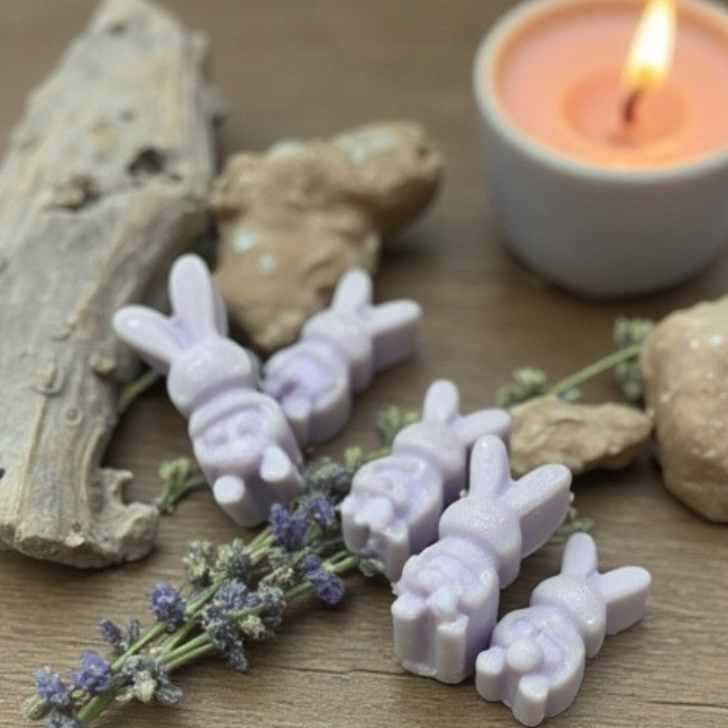 a picture of purple, bunny shaped wax melts laying by sprigs of lavender and pieces of drift wood